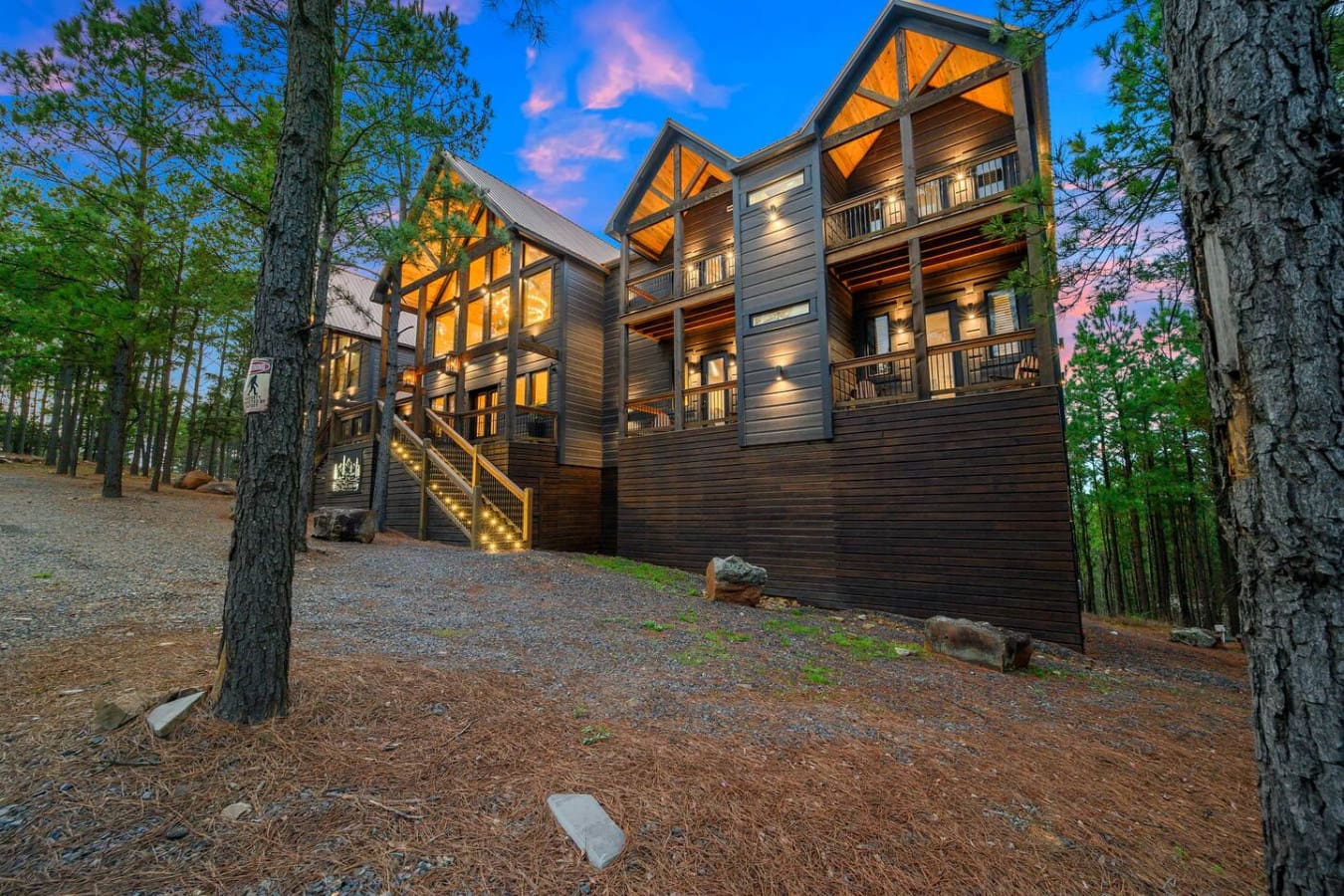 This stunning modern cabin nestled in the pines glows beautifully at dusk with soaring ceilings and wraparound decks.
