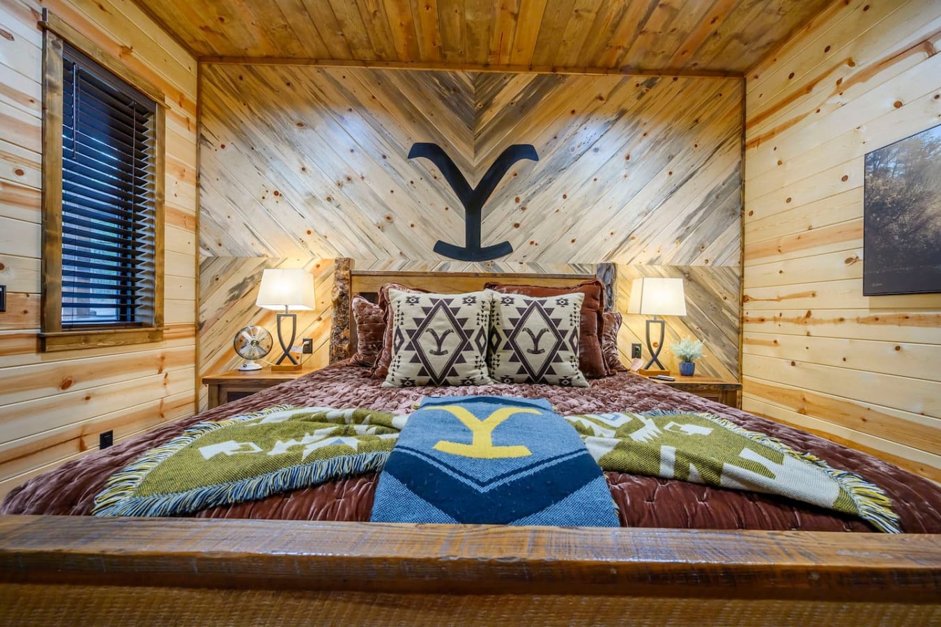 This cozy log cabin bedroom features a custom Y-branded accent wall and warm wood throughout with stylish Western-inspired bedding.