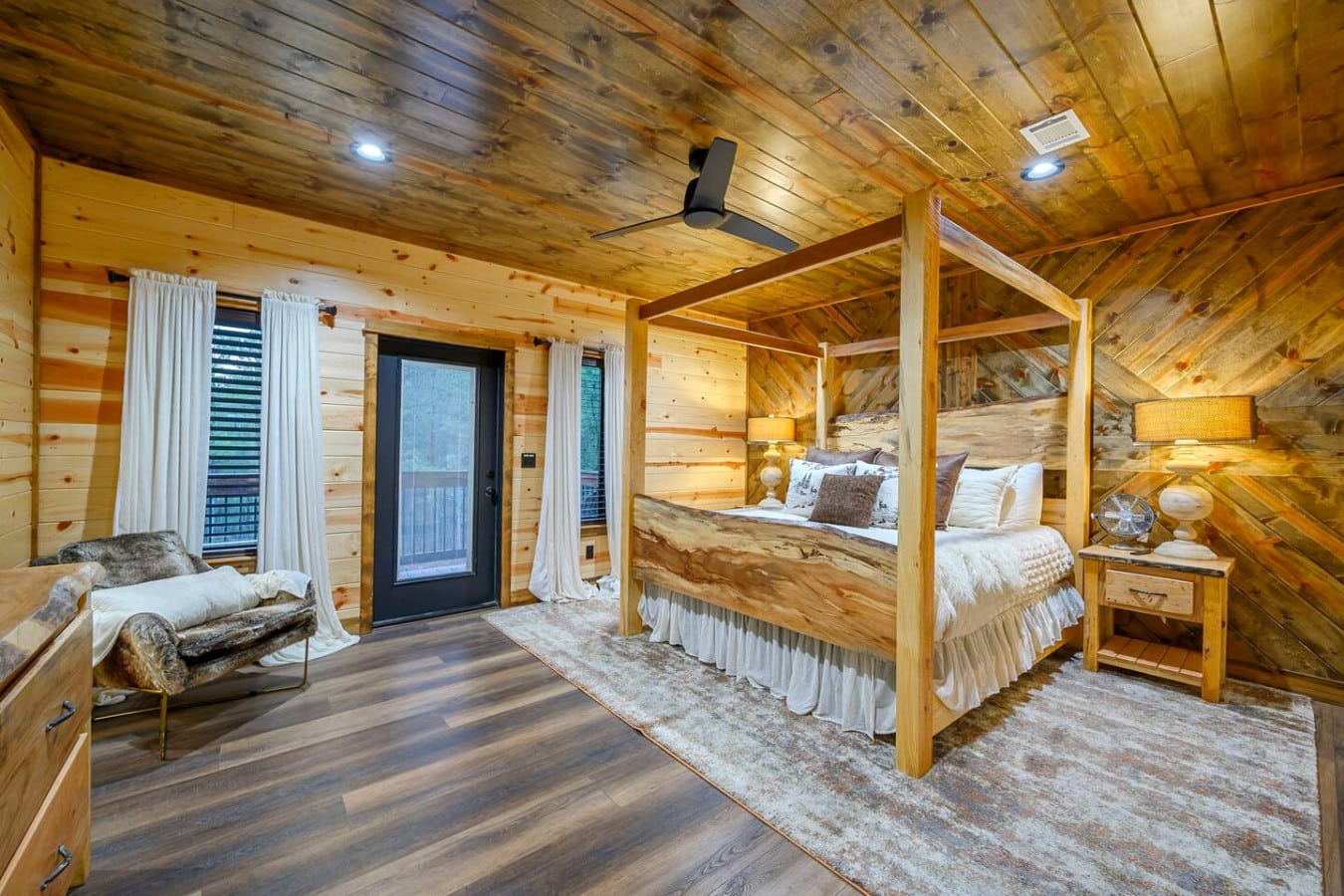 This gorgeous log bedroom features a massive four-poster bed, cozy seating area, and private balcony overlooking the mountains.