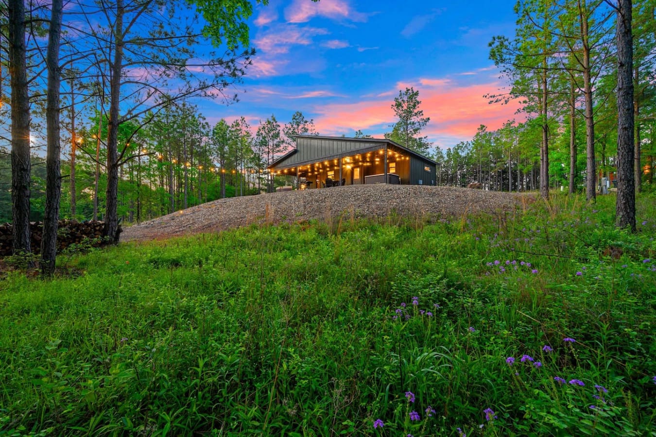 Watch this sleek modern cabin come alive as the sun sets behind the pines, casting that perfect golden glow across the gravel courtyard while the sky turns those dreamy shades of pink and blue.