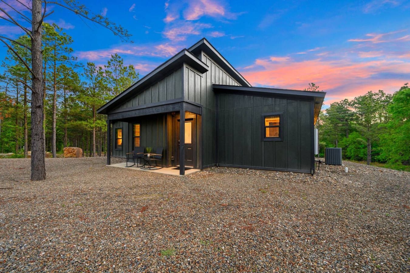 This sleek modern black cabin feels like your own hidden getaway tucked deep in the pines, with those warm interior lights glowing as the sky puts on a show overhead.