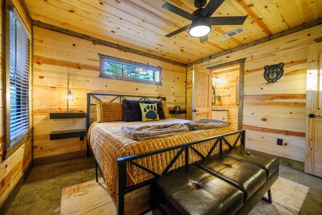 This bedroom is basically the perfect cabin retreat with those gorgeous wood walls, a black metal bed frame loaded with cozy blankets, and paw print pillows that add just the right touch of personality to the space.