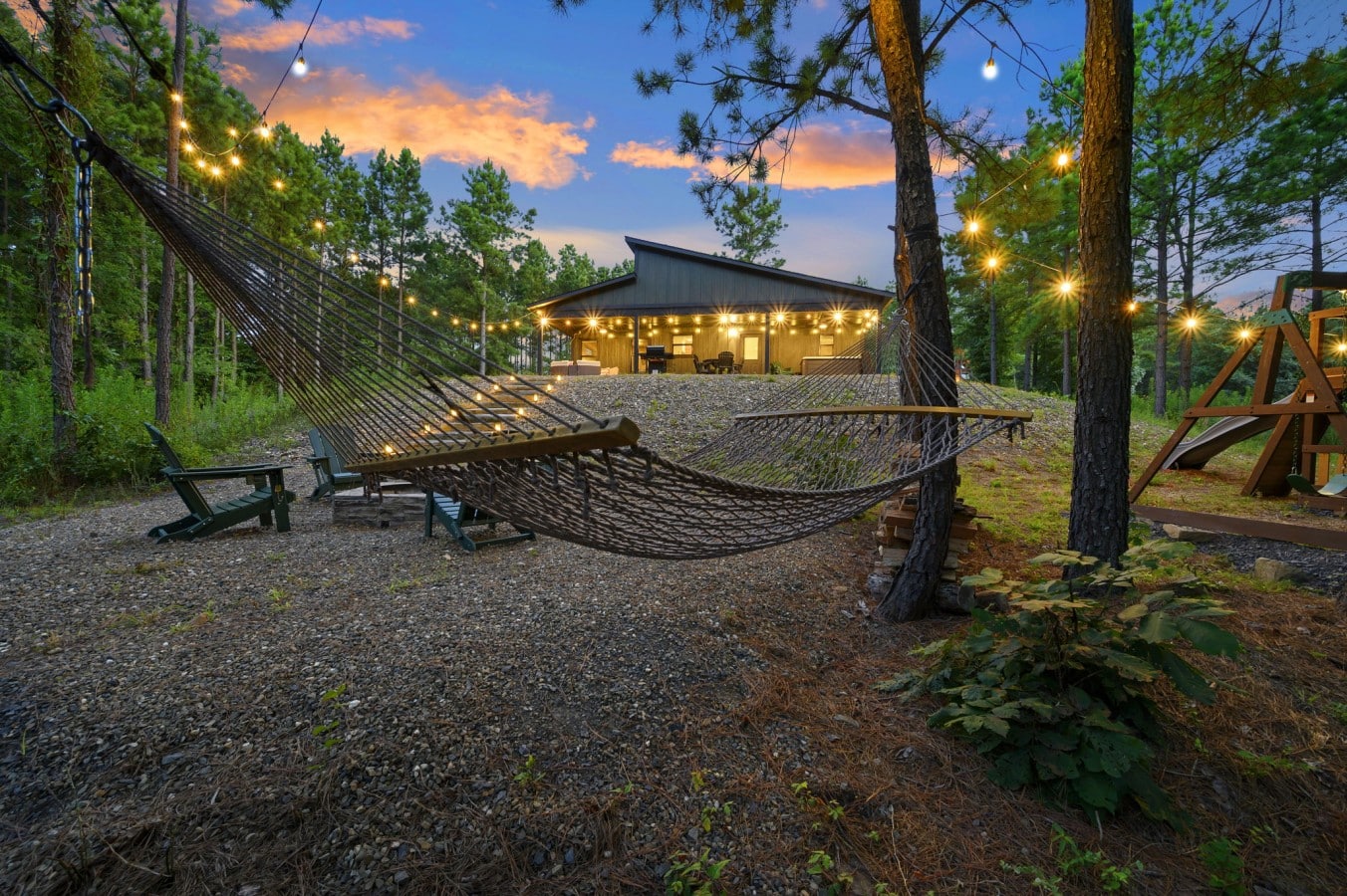 Fire pit lounge surrounded by trees and warm string lights.