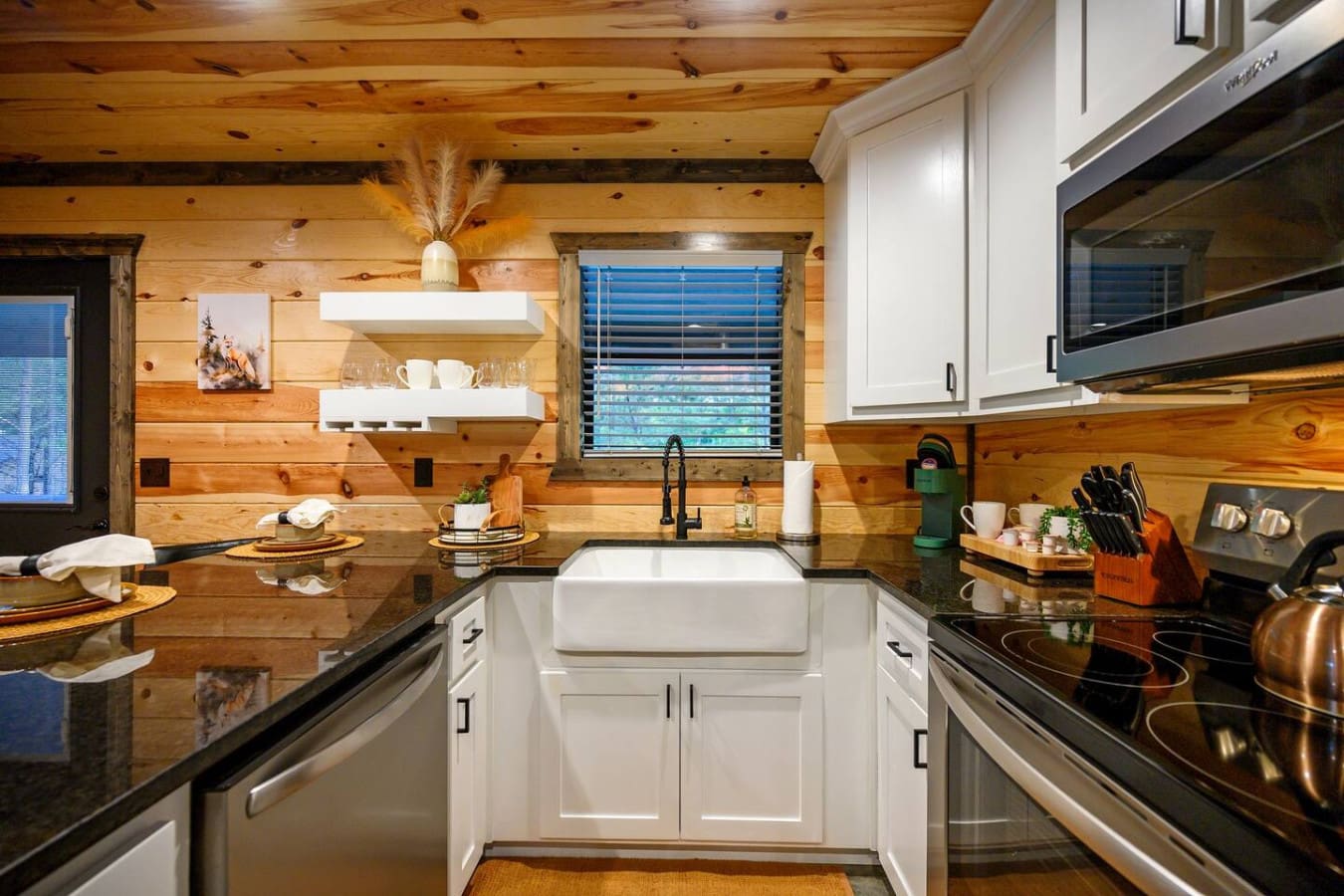 This kitchen is the perfect blend of rustic charm and modern convenience, with those crisp white cabinets and sleek black countertops looking right at home against all that warm knotty pine.