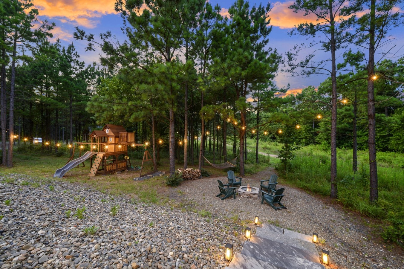 Fire pit and play area viewed from above in the wooded yard.