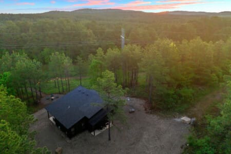 This sleek black cabin tucked deep in the forest feels like your own private hideaway, especially watching it light up as the sun dips behind those rolling pine-covered hills.