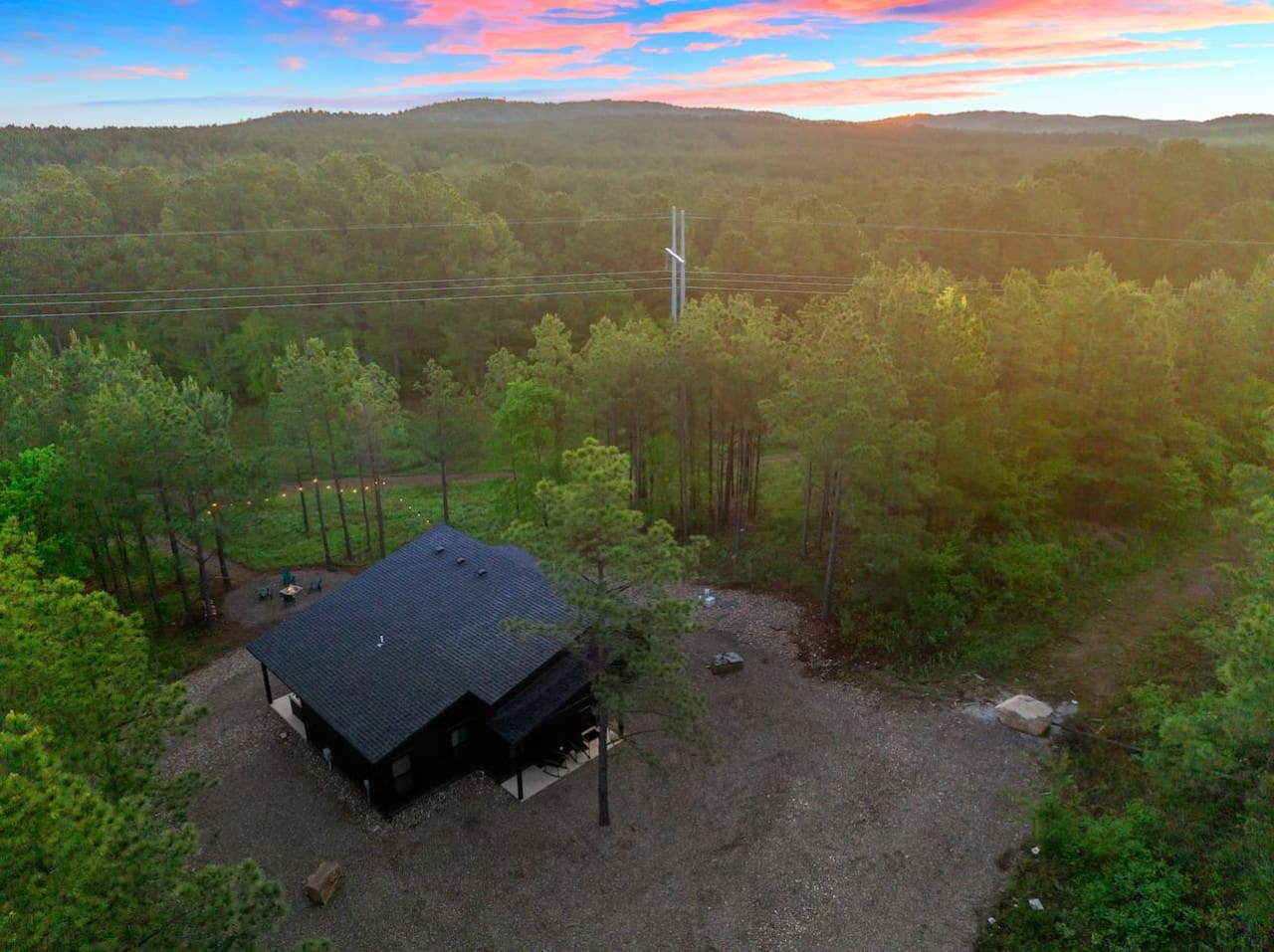 This sleek black cabin tucked deep in the forest feels like your own private hideaway, especially watching it light up as the sun dips behind those rolling pine-covered hills.