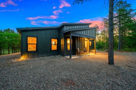 This sleek modern cabin tucked into the pines is giving serious "my own private forest escape" energy, especially when it's all lit up like this against that gorgeous twilight sky.