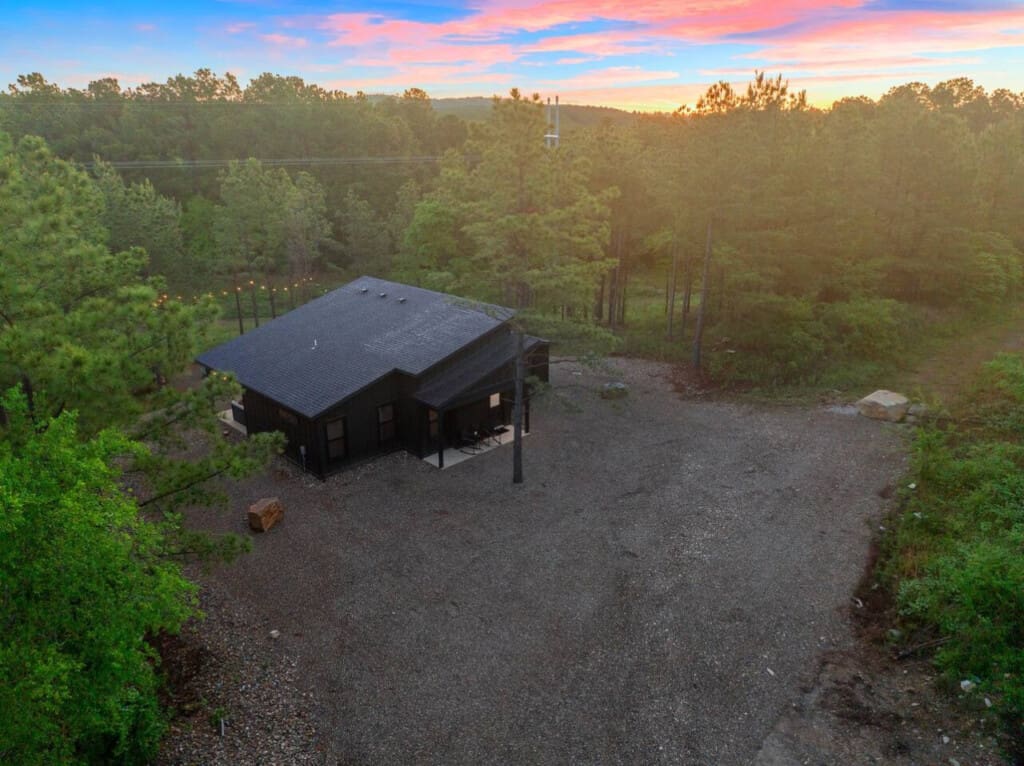 This sleek black cabin nestled in the pines feels like your own completely private forest escape, especially as the sunset paints the sky in those perfect shades of pink and blue.