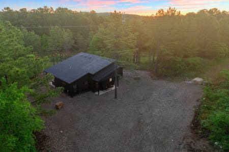 This sleek black cabin nestled in the pines feels like your own completely private forest escape, especially as the sunset paints the sky in those perfect shades of pink and blue.