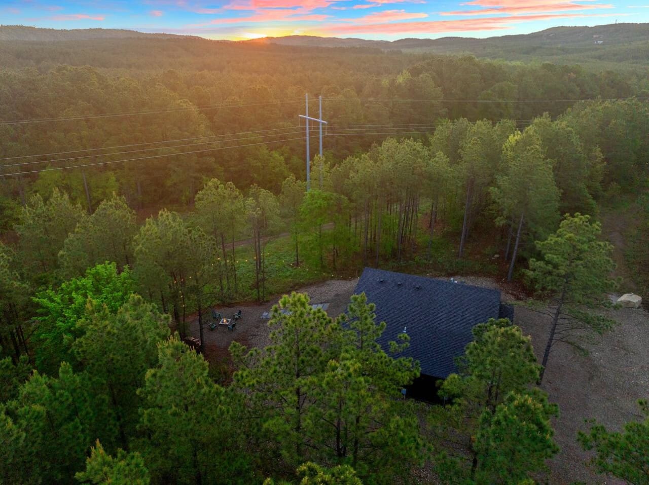 Wake up to this—your own modern cabin nestled in a sea of towering pines with the sunrise painting the sky in those perfect peachy-pink shades while the forest stretches out endlessly in every direction.