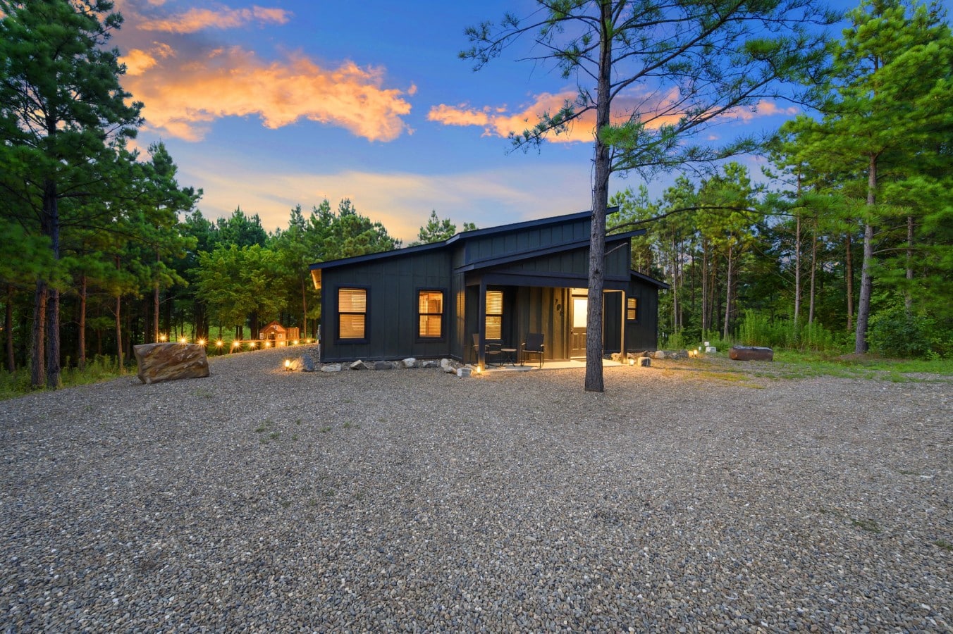 Welcoming front approach with cabin sign, gravel drive, and sunset sky.