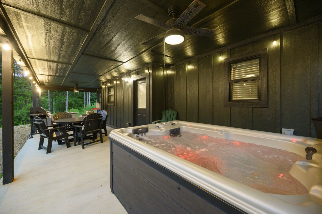 Hot tub beside the covered outdoor dining area and wooded backdrop.
