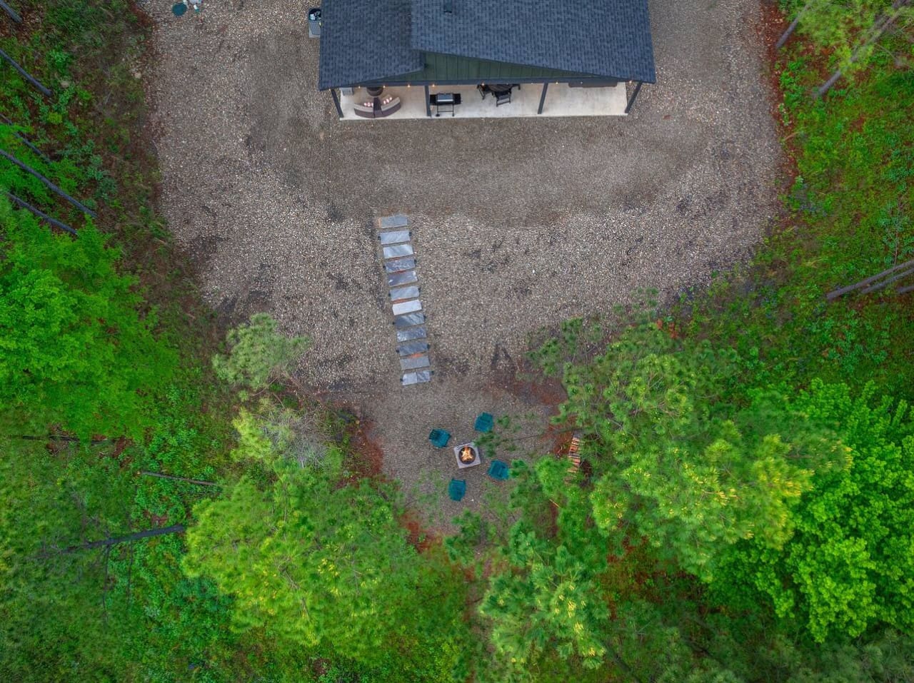 From above, you can see exactly why this place is so special—a cozy modern cabin nestled in the pines with a fire pit, stepping stones, and plenty of gravel space to just breathe and take it all in.