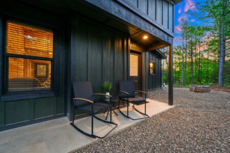 Your own private forest retreat is waiting with those cozy chairs on the patio, warm cabin glow spilling out into the evening, and nothing but tall pines surrounding you as far as the eye can see.