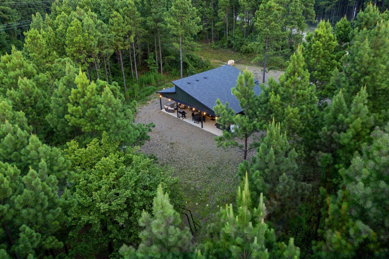 Drone view of the cabin roofline, driveway, and surrounding pines.
