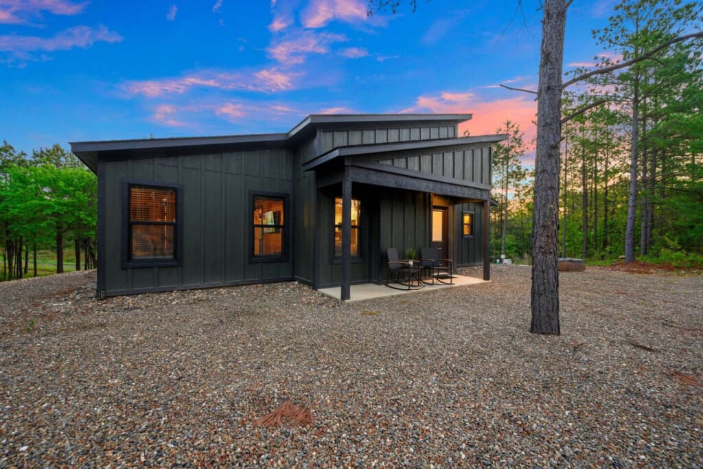 This sleek modern cabin tucked into the pines looks absolutely magical as twilight settles in and those interior lights glow against the forest backdrop.