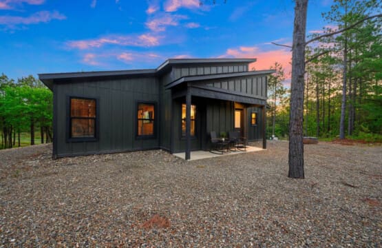 This sleek modern cabin tucked into the pines looks absolutely magical as twilight settles in and those interior lights glow against the forest backdrop.