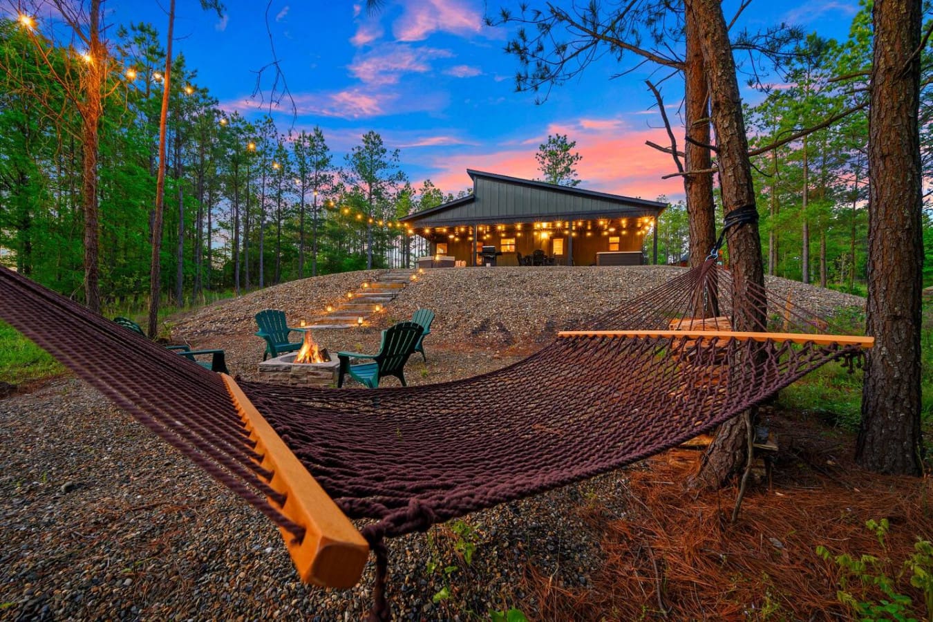 Picture yourself swaying in a hammock at sunset with nothing but tall pines, a crackling fire pit, and that stunning modern cabin glowing in the distance.