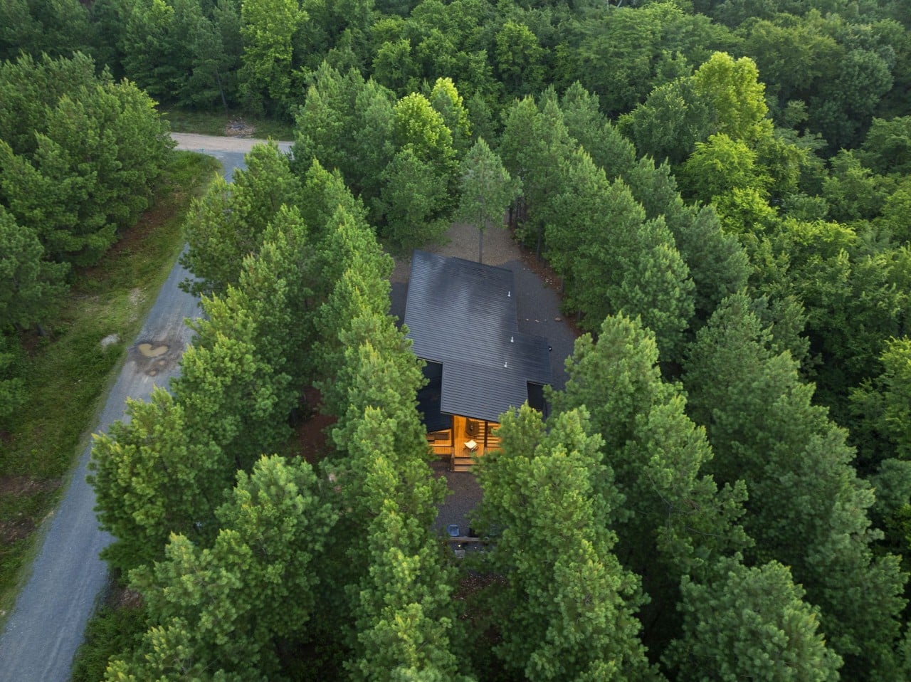 Aerial view showing the cabin roofline, drive, and private wooded setting.