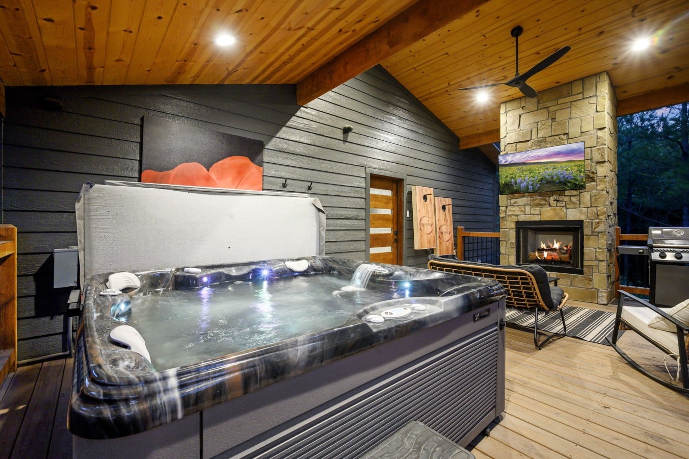 Covered deck view with hot tub, fireplace, TV, and lounge space together.