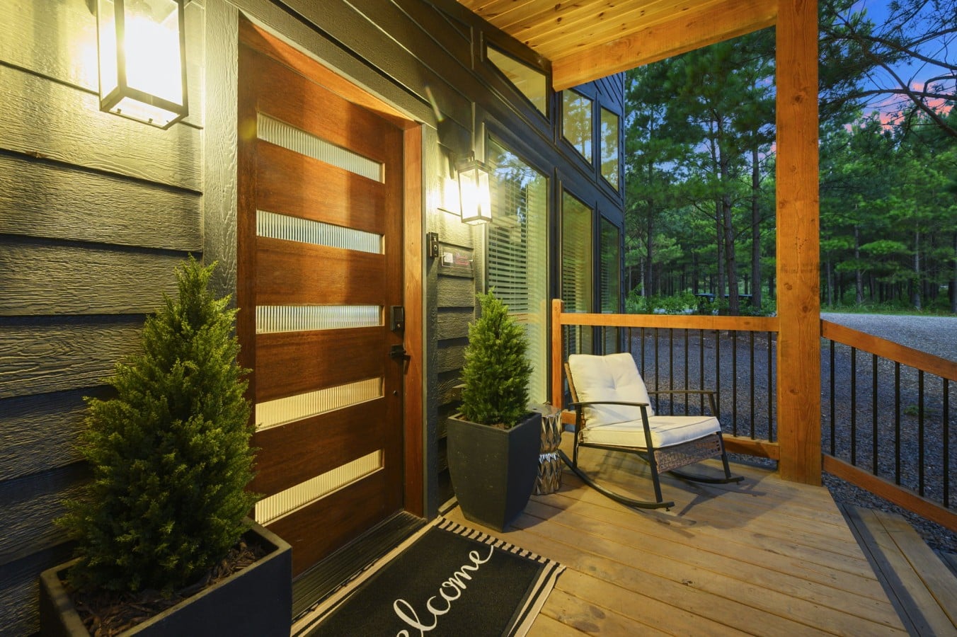 Welcoming porch entry with warm lighting and wooded views.