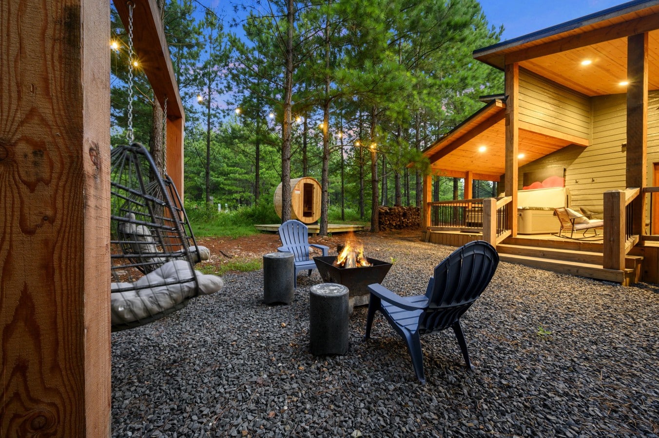 Fire pit lounge with cabin, sauna, and forest backdrop.