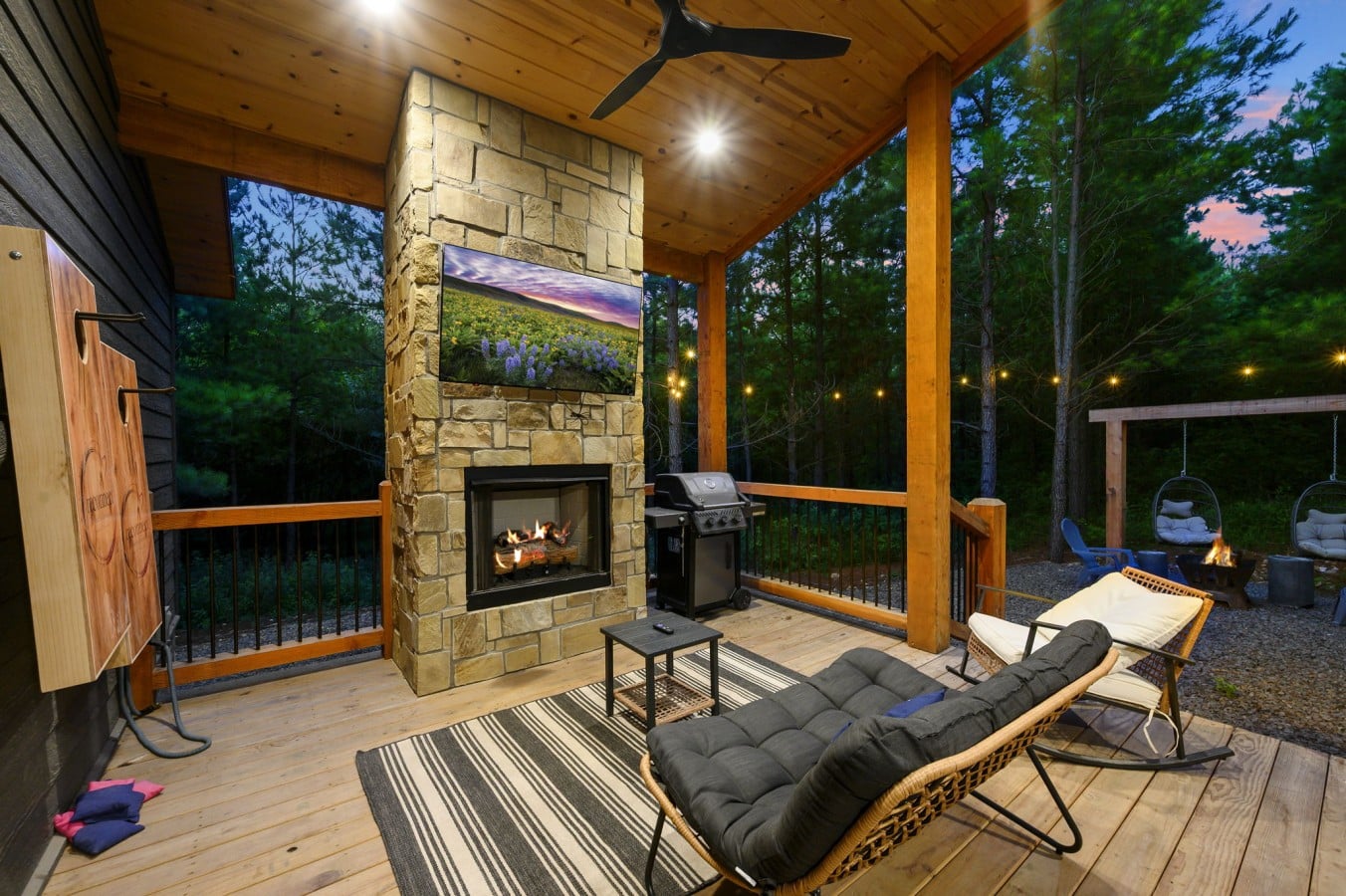 Covered deck lounge chairs facing the fireplace and wooded view.