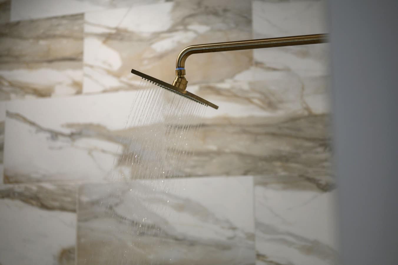 A gold rain shower head cascading over marble — because you deserve this every morning.