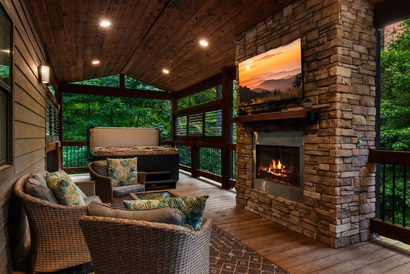 Cozy deck seating beside the outdoor fireplace and wooded backdrop.