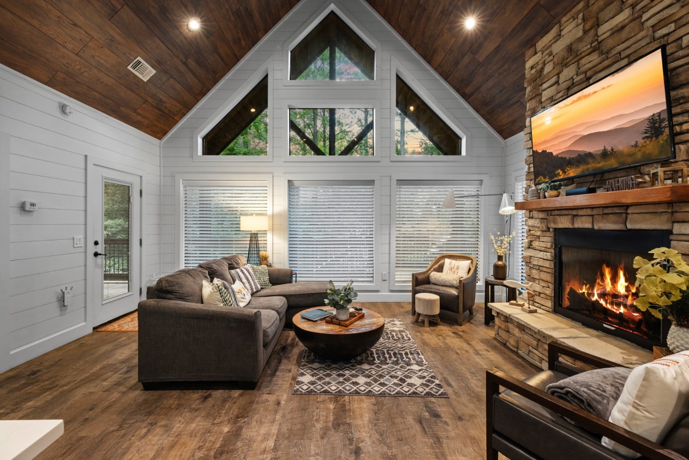Open living room framed by tall windows and a stone fireplace.
