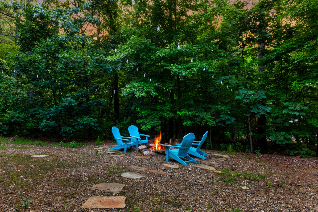 Blue Adirondack seating around the fire pit under the Broken Bow trees.