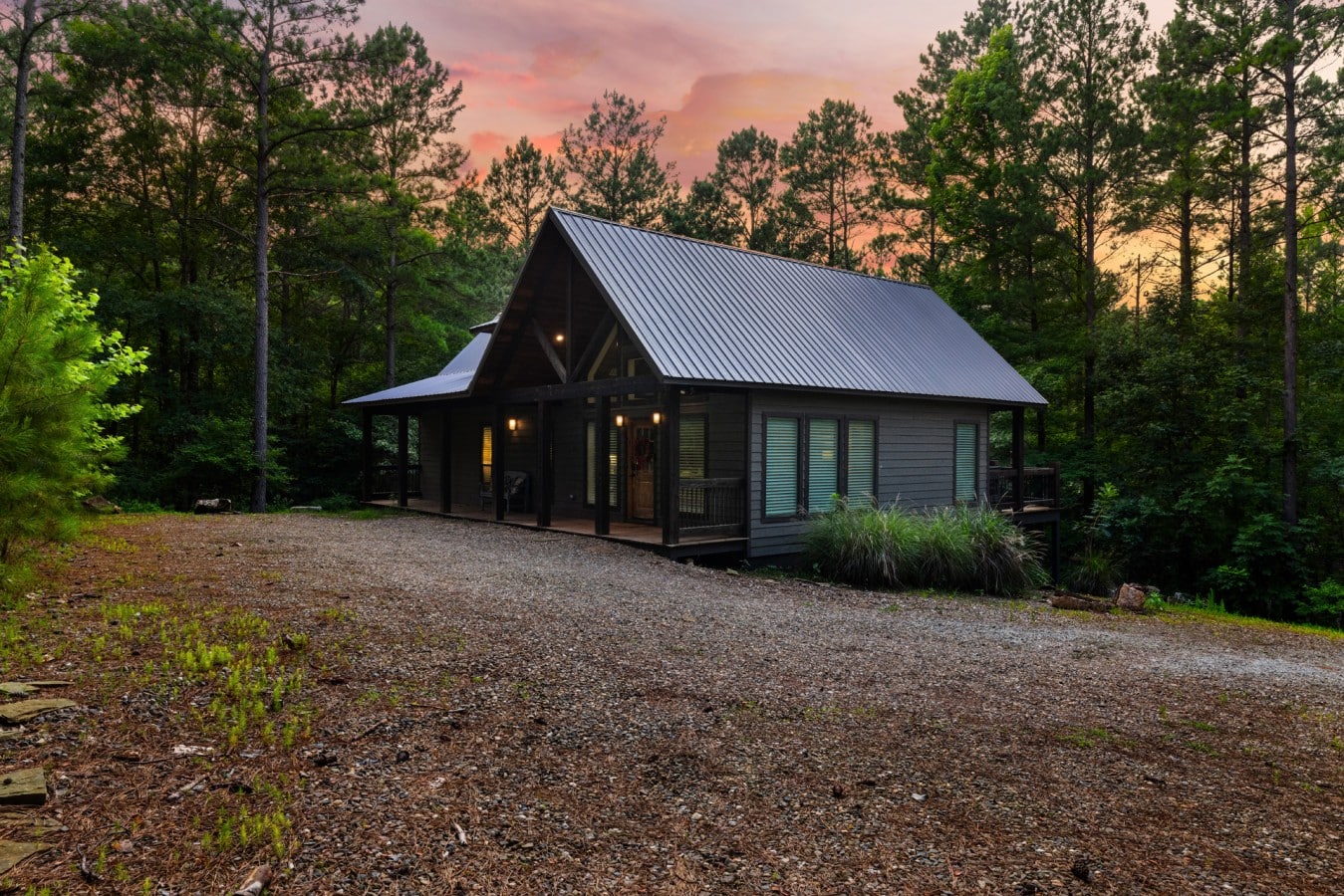Front exterior and gravel drive with a peaceful wooded backdrop.