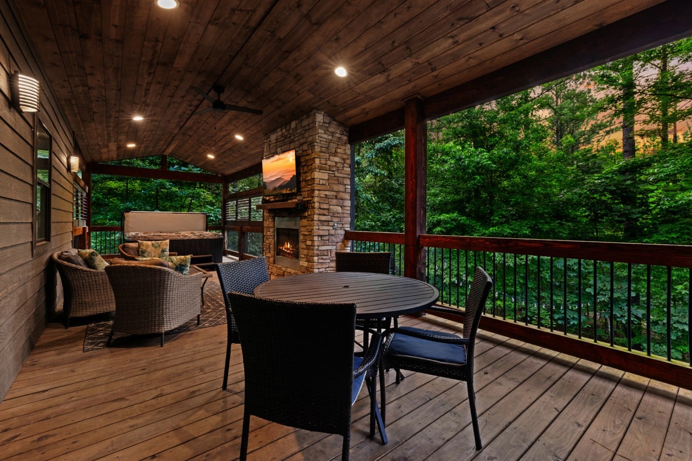 Covered deck lounge with fireplace, dining space, and forest views.