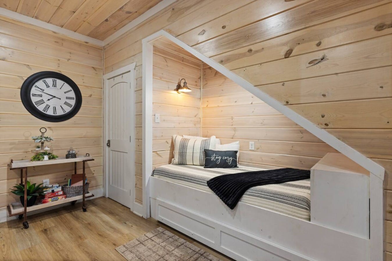 Daybed nook with simple decor, wall clock, and cabin-style lighting.
