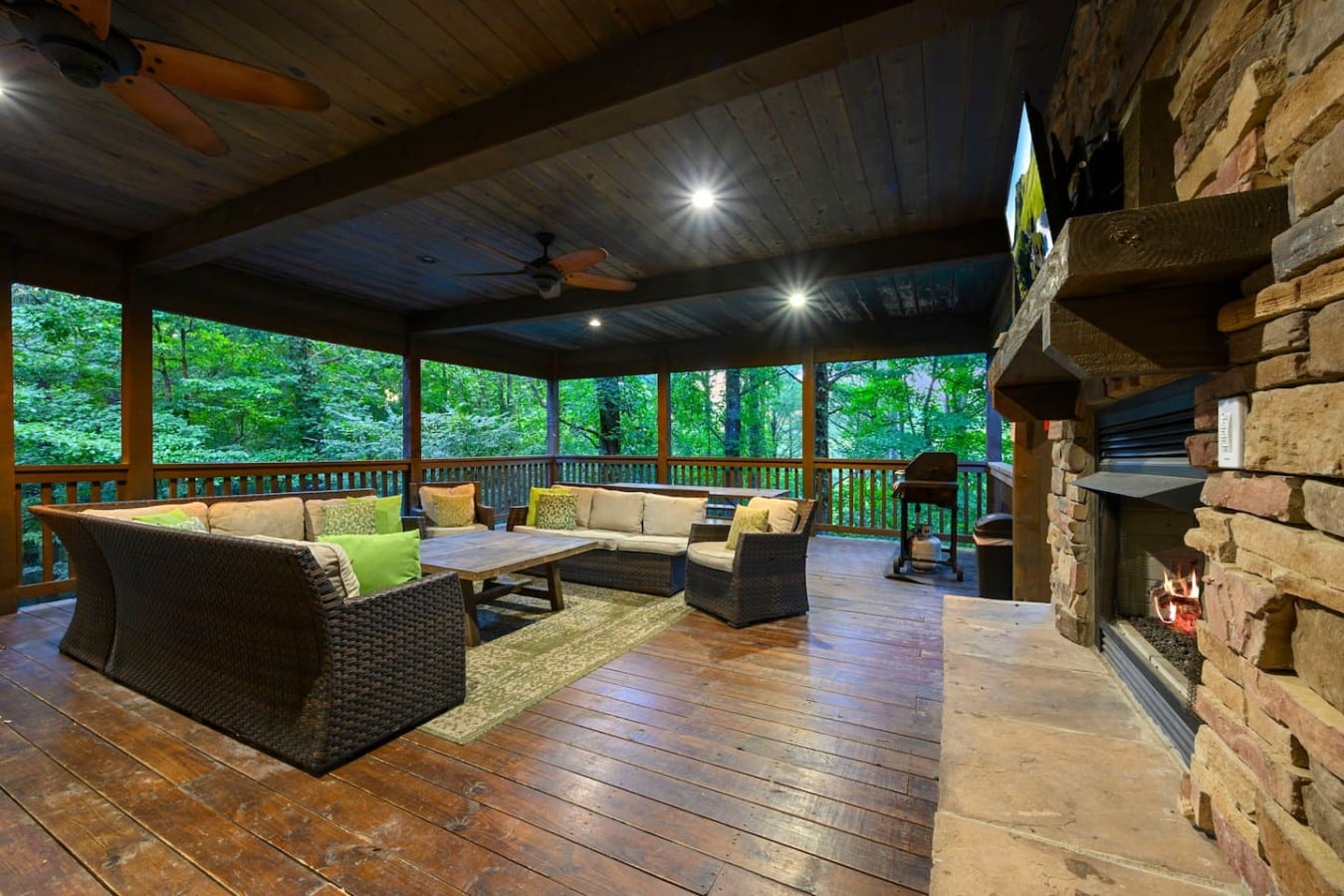 Covered deck lounge with TV, fireplace, and forest views.