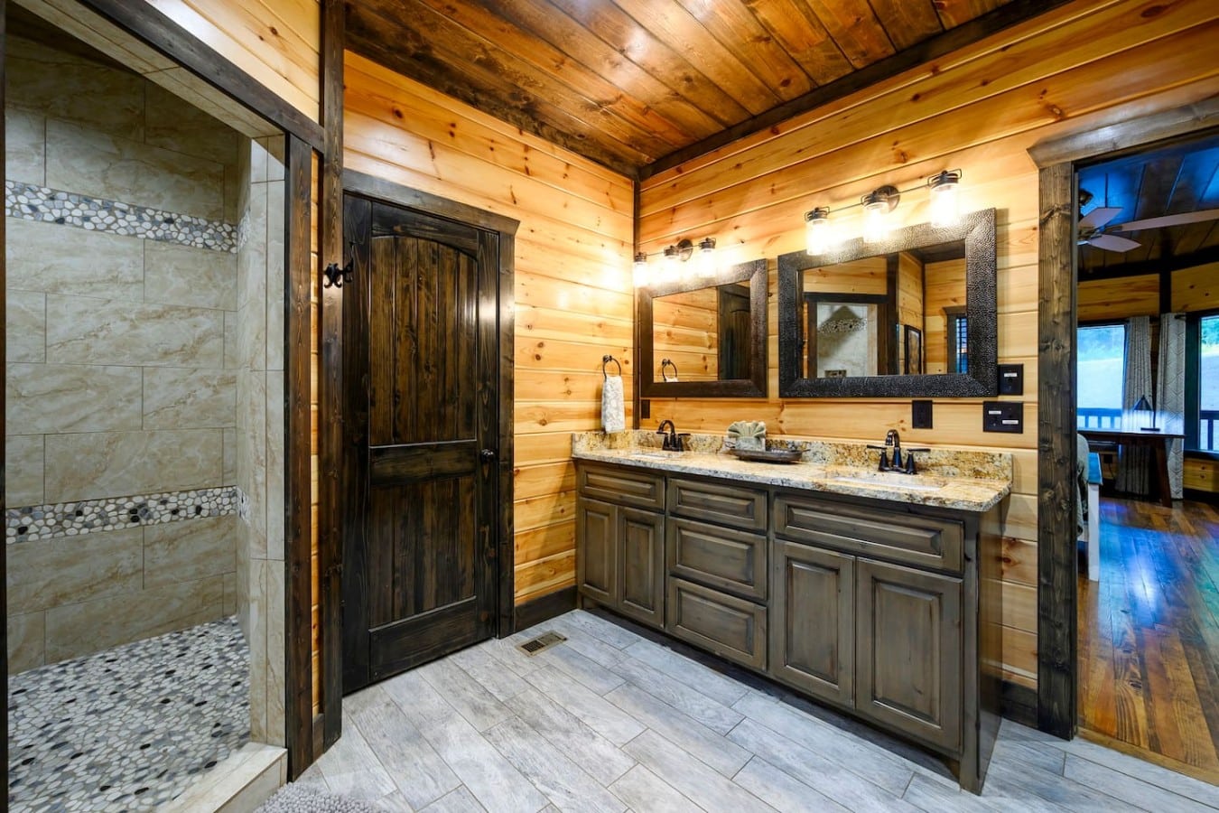 Double vanity bathroom with granite counters and rustic wood finishes.
