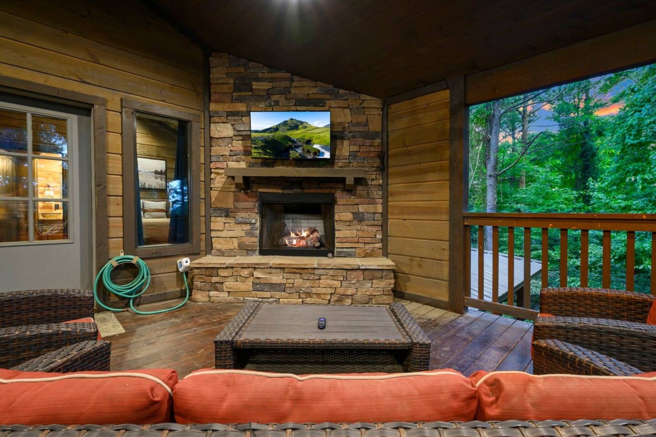 Outdoor fireplace lounge with TV and comfortable seating.