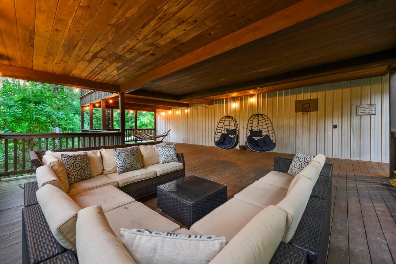 Covered deck sectional with hanging chairs and wooded backdrop.