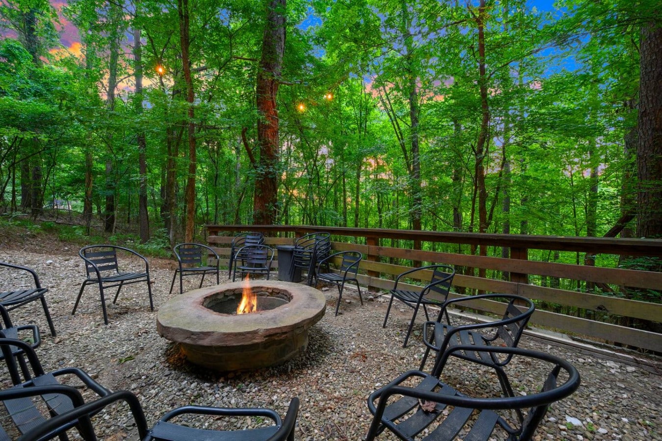 Fire pit seating surrounded by trees and string lights.