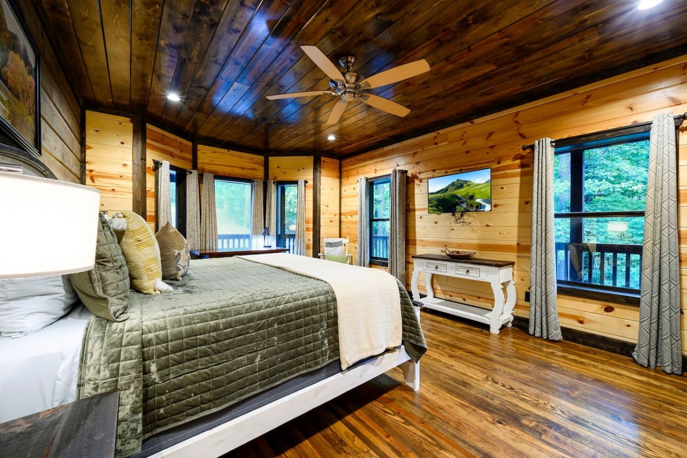 Primary king suite with TV, ceiling fan, and wooded deck access.