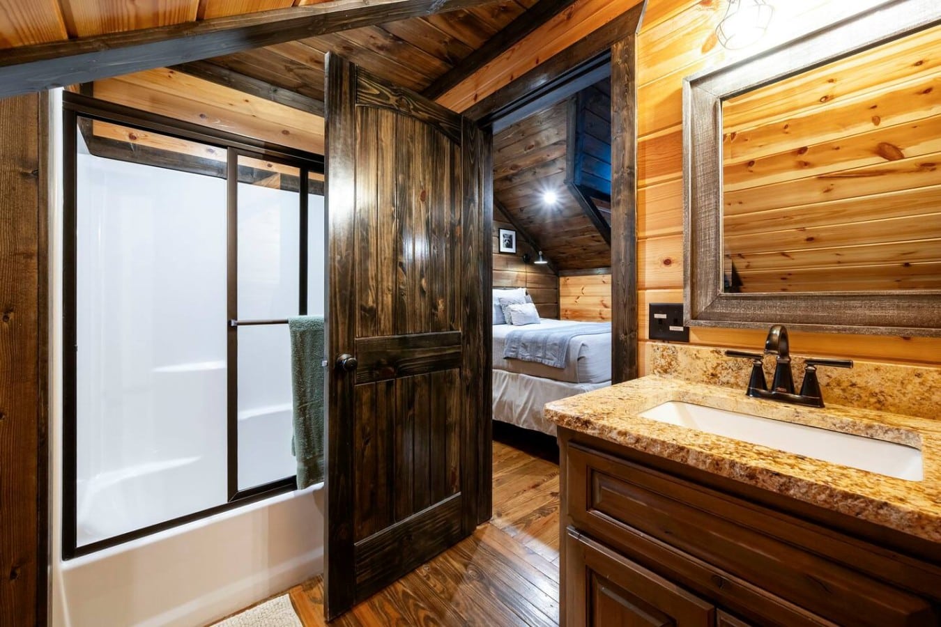 Shower and vanity area with warm wood walls and black fixtures.