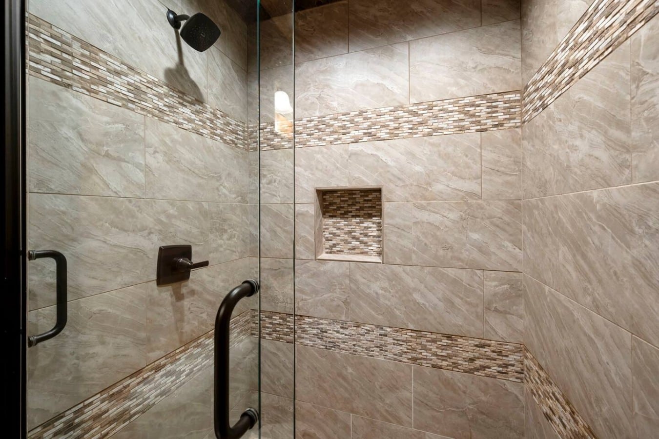 Tile shower with glass door, niche, and modern black fixtures.