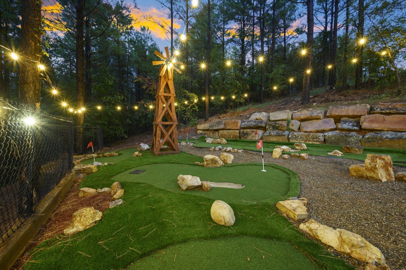 A wooden windmill, boulder hazards, and string lights make every putt an adventure.