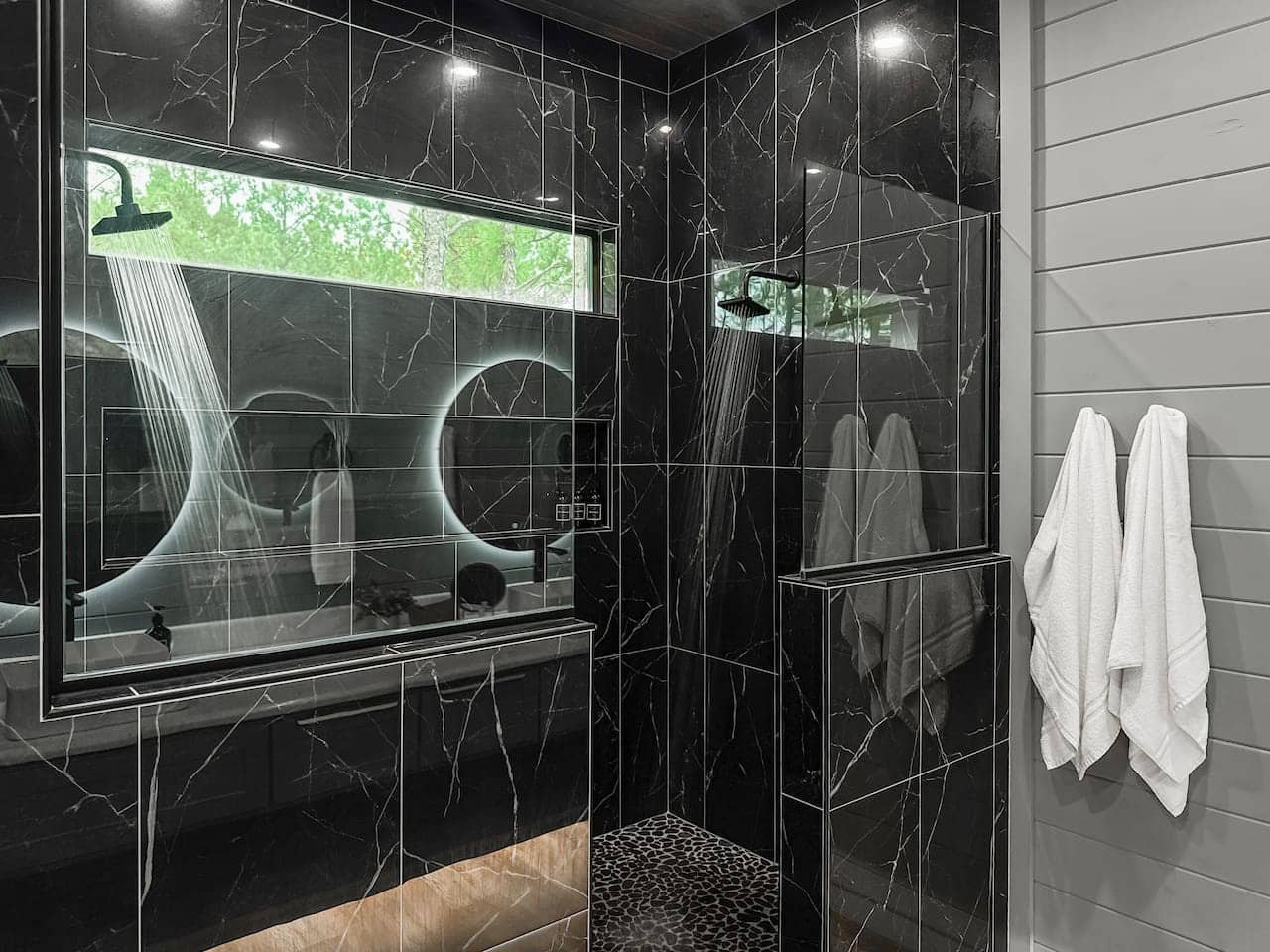 Rinse off under a rain head in a floor-to-ceiling marble shower with a forest window.