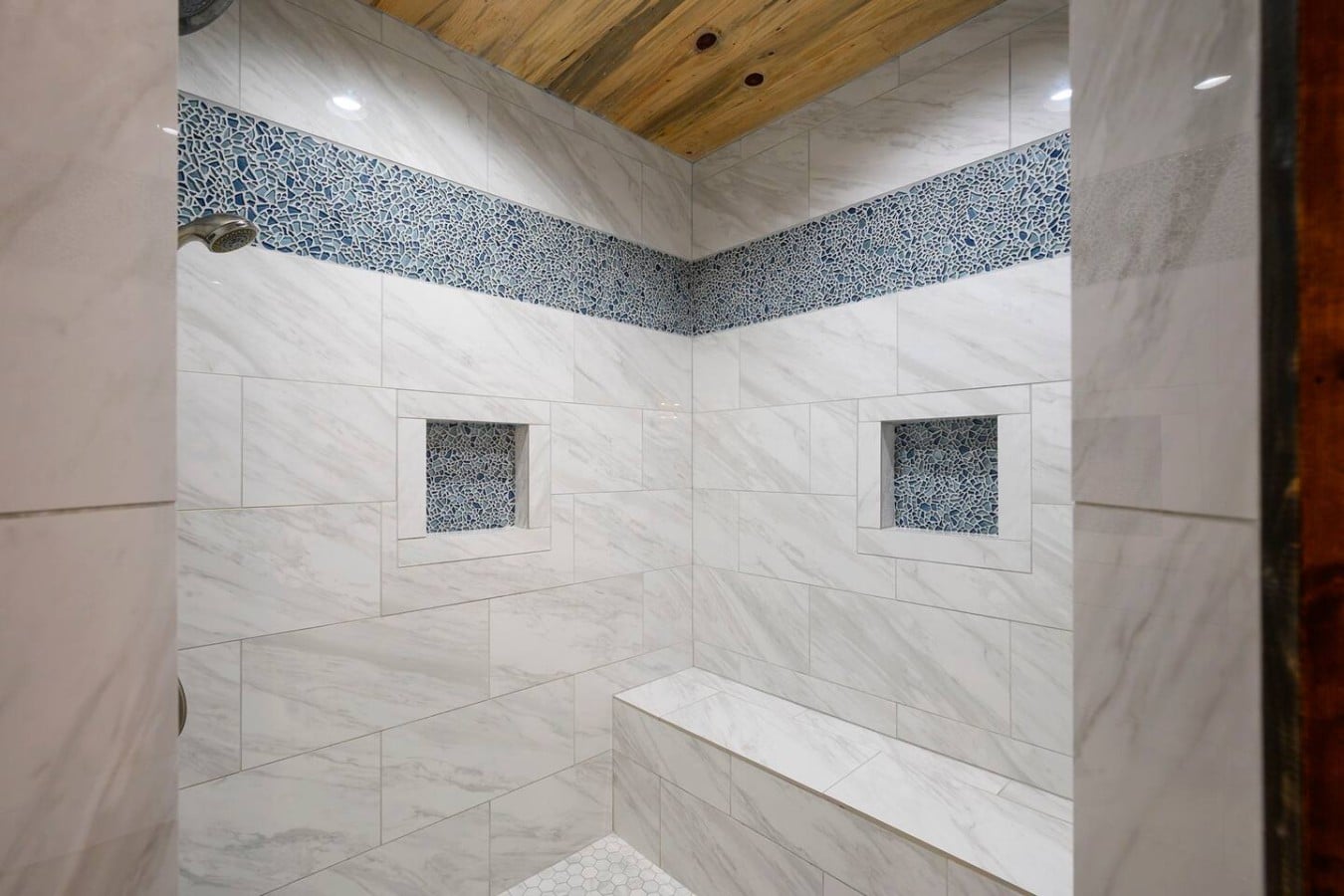 A bench seat, dual niches, and warm wood ceiling turn every shower into a spa moment.