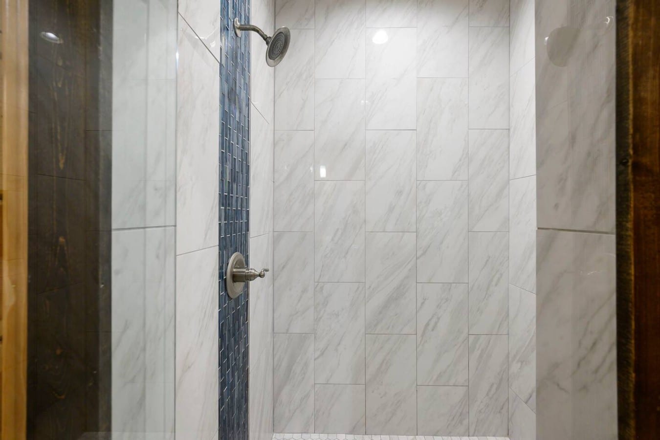 Refresh under a rainfall showerhead surrounded by sleek marble-look tile.