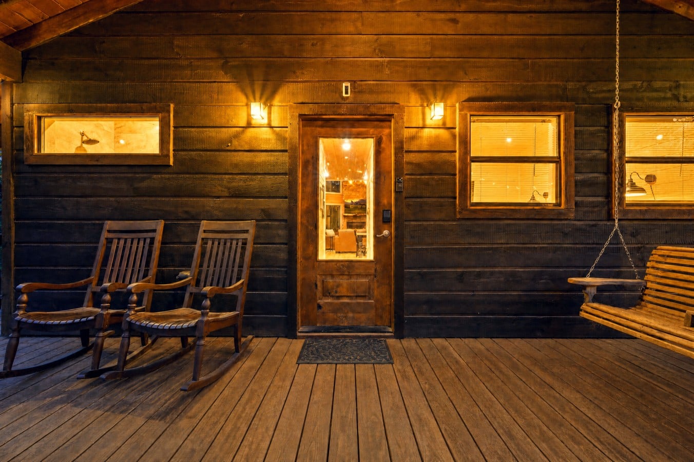 A porch swing, two rocking chairs, and a glowing front door — welcome to your getaway.